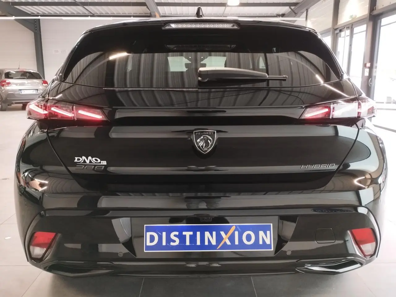 Vue arrière d'une Peugeot 308 hybride noire métallisée avec feux arrière LED en forme de griffes et logo lion central.