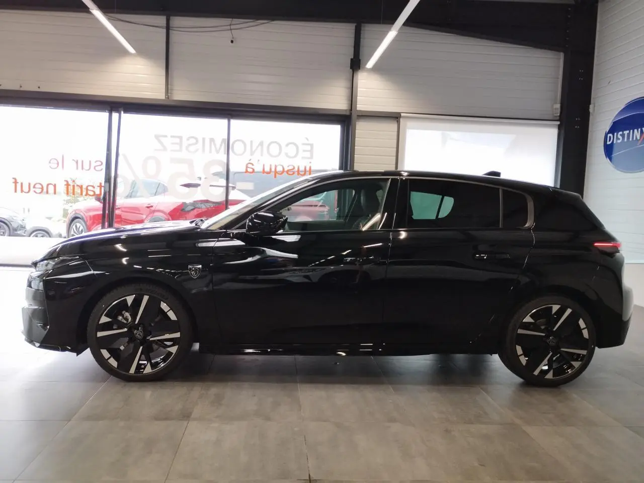 Profil droit d'une Peugeot 308 noire métallisée avec jantes alliage bi-tons et détails noirs brillants en intérieur showroom.