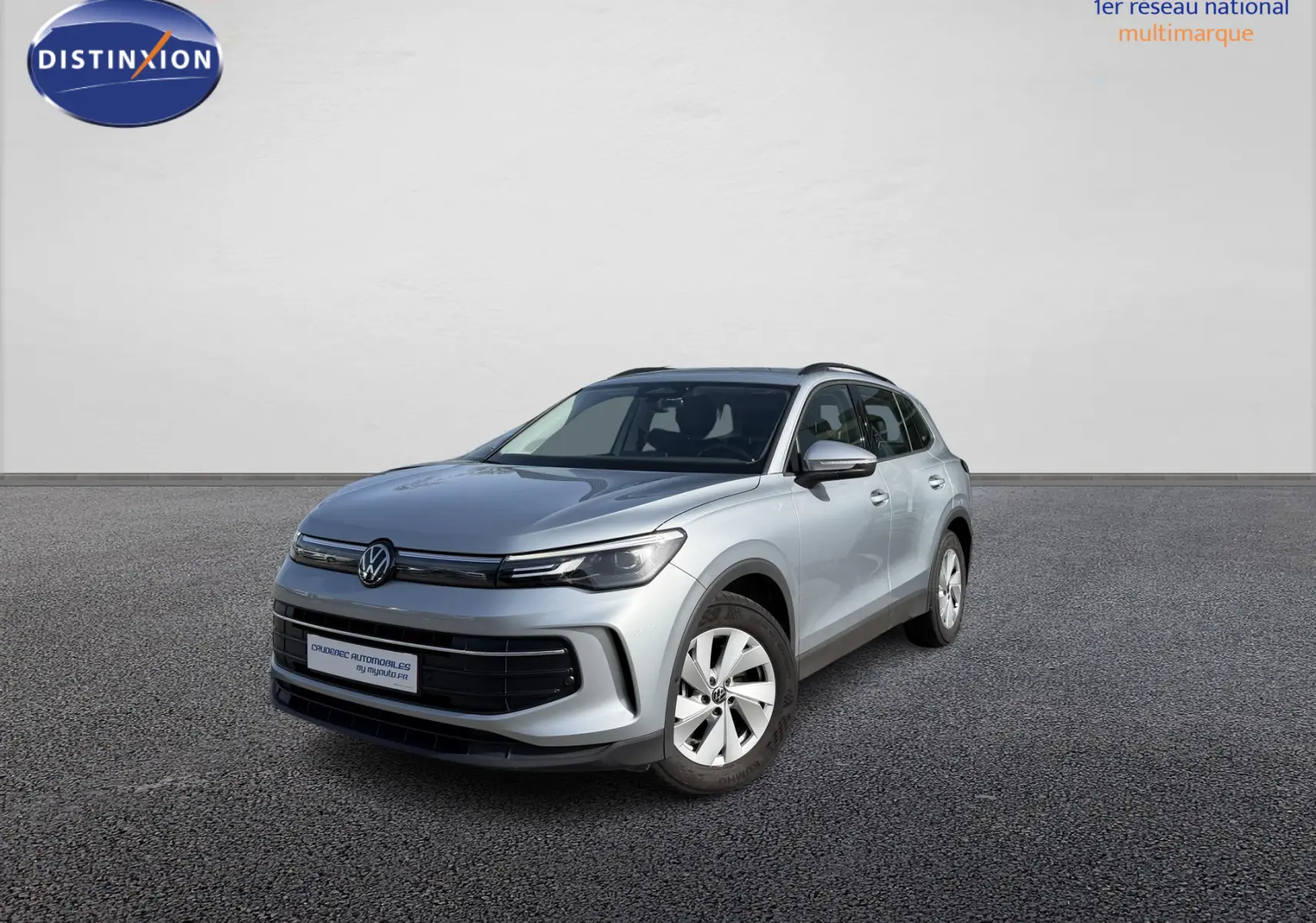 Volkswagen Tiguan gris en 3/4 avant droit devant un concessionnaire, avec jantes alliage et calandre noire.