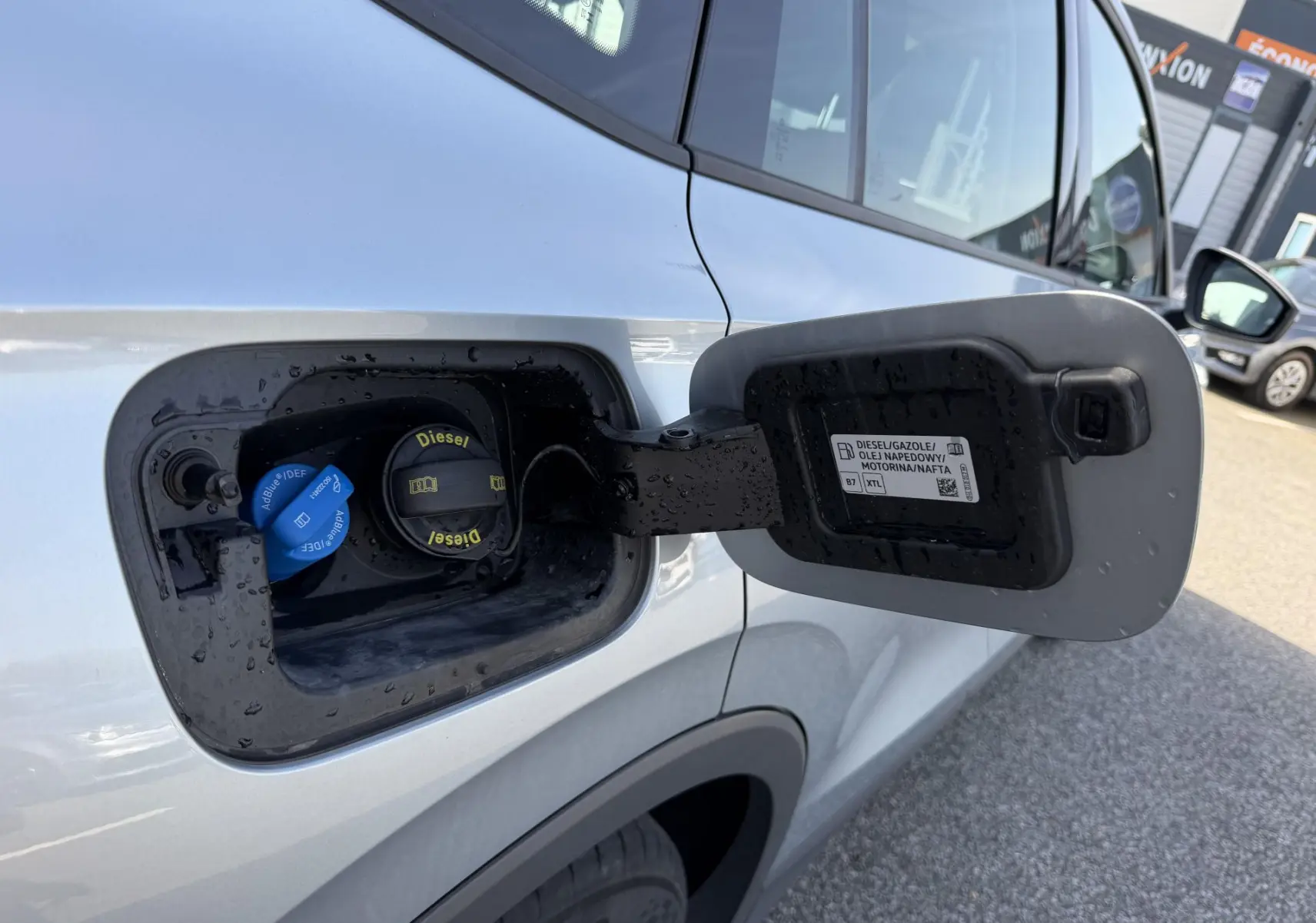Vue rapprochée de la trappe à carburant ouverte côté gauche du Volkswagen Tiguan gris, montrant les bouchons Diesel et AdBlue.