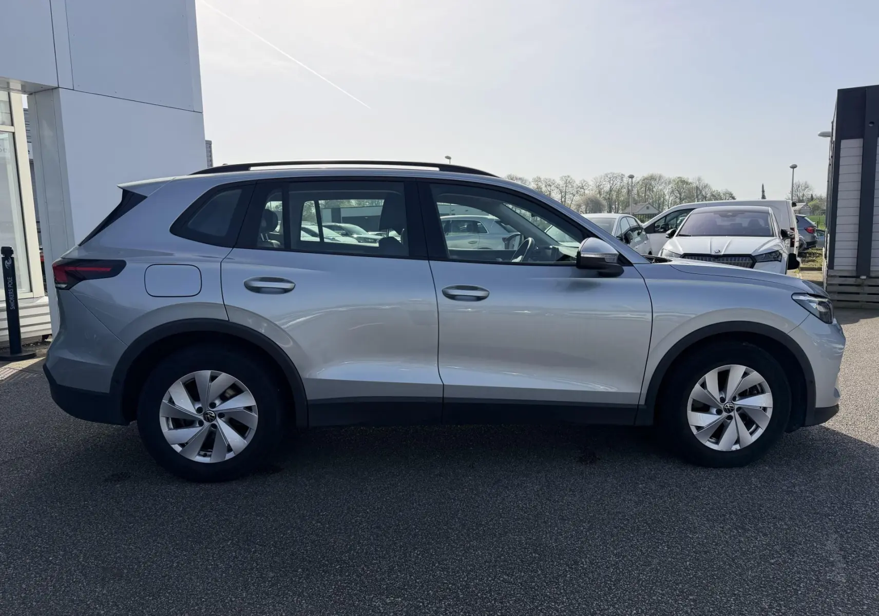 Vue de profil côté gauche d'un Volkswagen Tiguan gris 2025 garé en extérieur, avec jantes alliage et toit noir.
