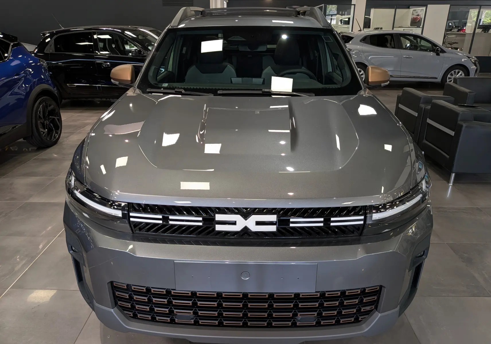 Vue avant du Dacia Bigster Hybrid-G 150 4x4 Extrême gris schiste avec calandre noire et détails cuivrés en showroom.