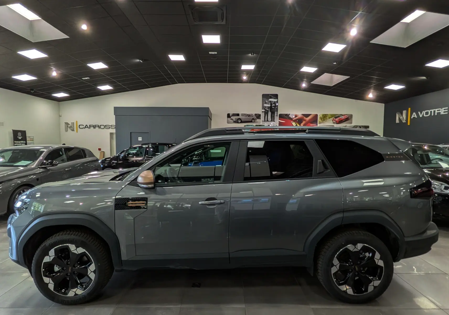 Profil droit du Dacia Bigster Hybrid-G 150 4x4 gris schiste, avec jantes bicolores et rétroviseurs cuivrés.