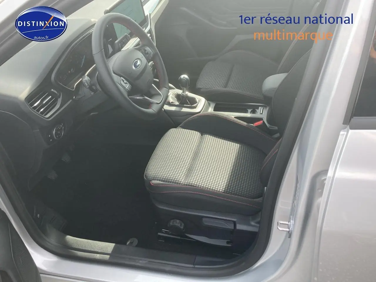 Vue intérieure côté conducteur de la Ford Focus 2025 gris, volant 3 branches avec coutures rouges et boîte manuelle.