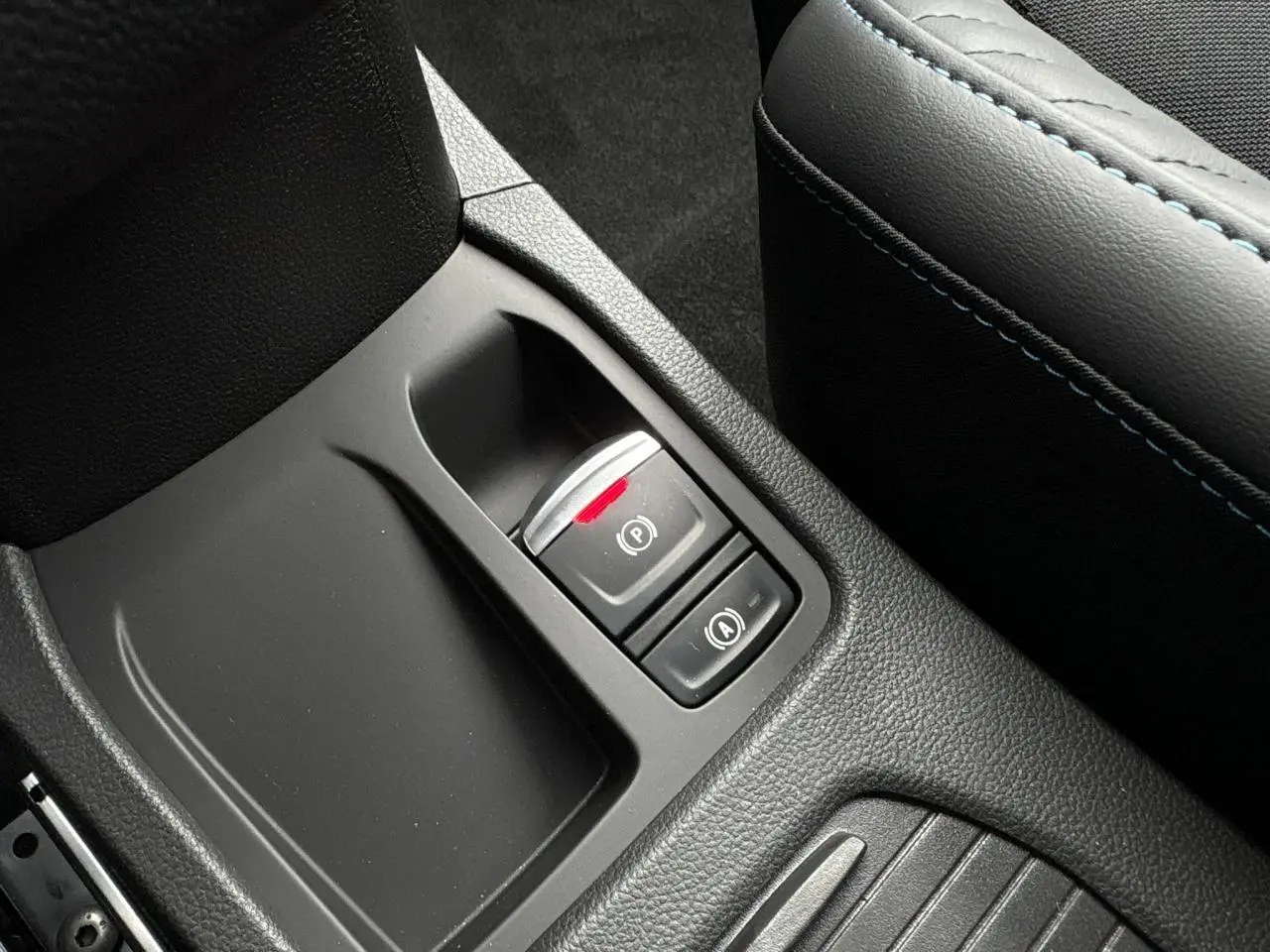 Gros plan sur la console centrale noire avec frein de parking électrique et accoudoir gris à surpiqûres bleues Renault Clio 2025.