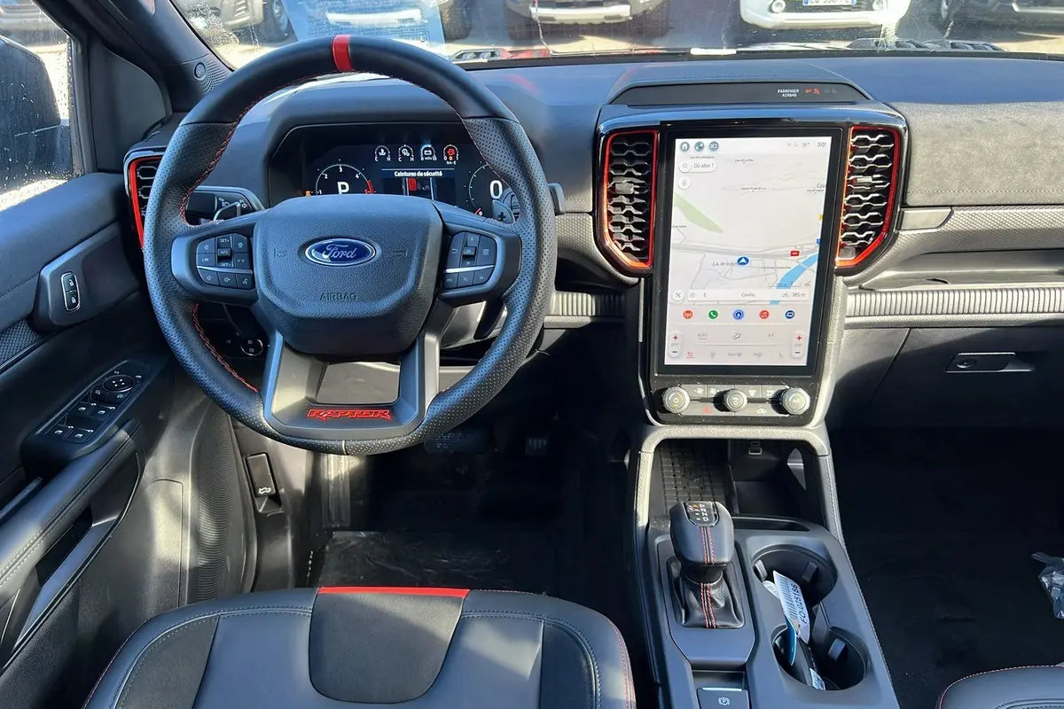 Vue intérieure avant du Ford Ranger Raptor noir, volant cuir avec surpiqûres rouges et écran tactile vertical.