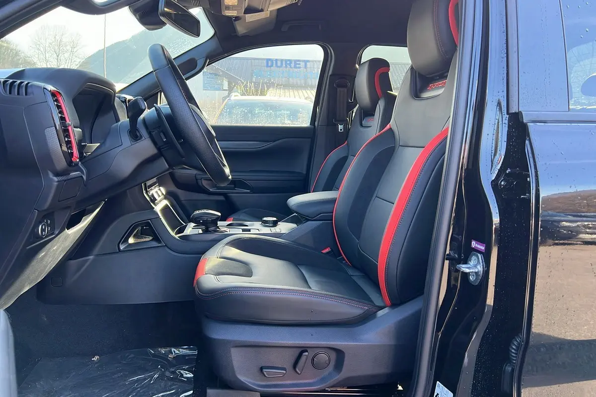Intérieur côté conducteur du Ford Ranger Raptor 2025 noir, sièges sport cuir noirs avec surpiqûres rouges et volant multifonctions.
