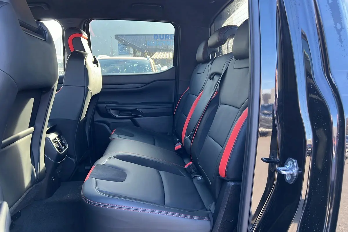 Vue latérale intérieure arrière droite du Ford Ranger Raptor noir absolu, sièges cuir noirs avec surpiqûres rouges.