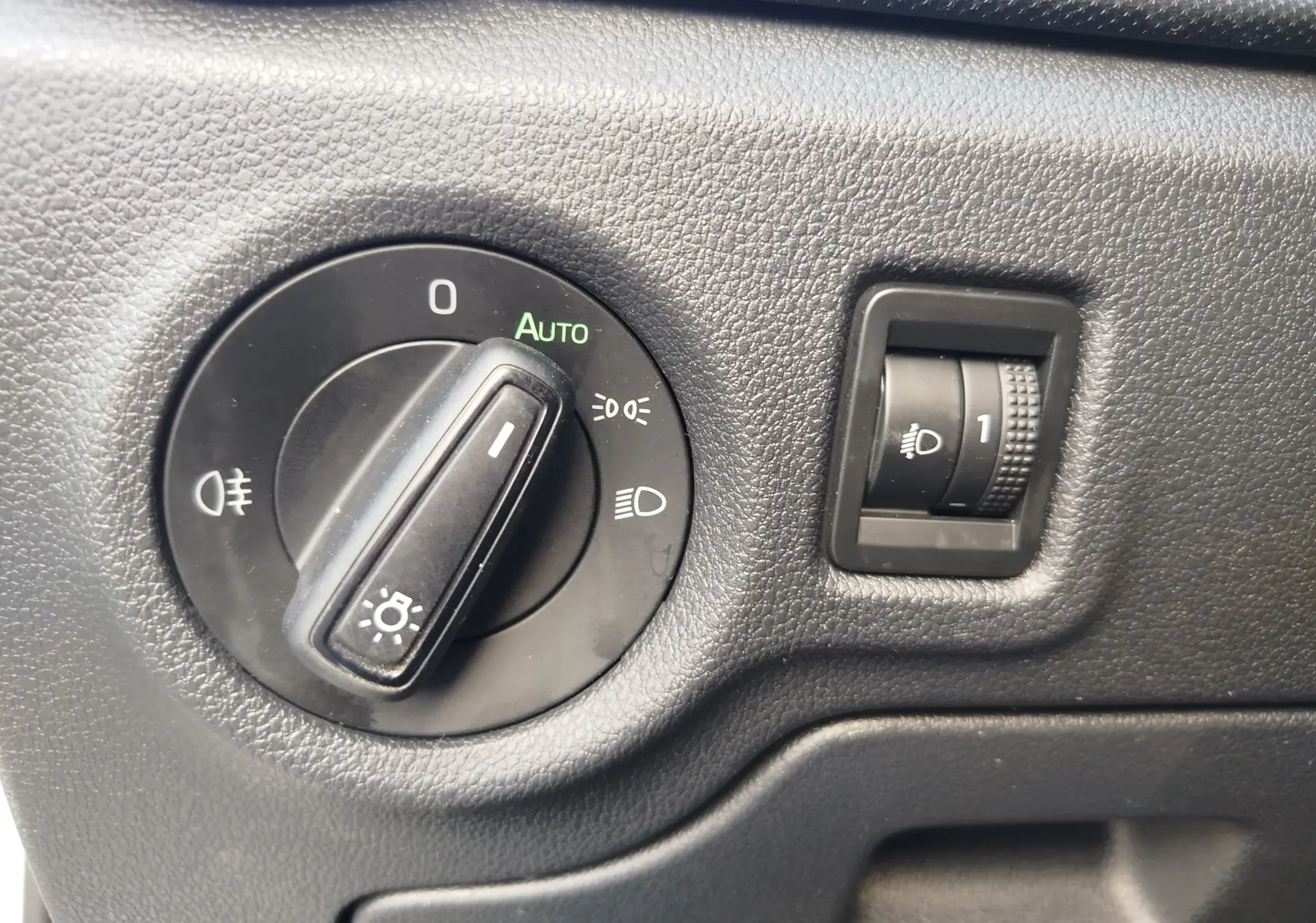 Gros plan sur le sélecteur de phares et le réglage d’intensité lumineuse du tableau de bord noir d’une Skoda Fabia blanche.