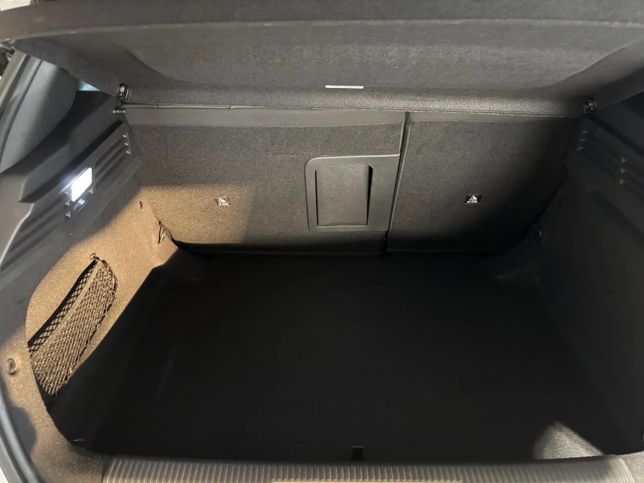 Coffre ouvert de la Peugeot 308 blanche, vue intérieure montrant un espace de rangement noir et un filet latéral.
