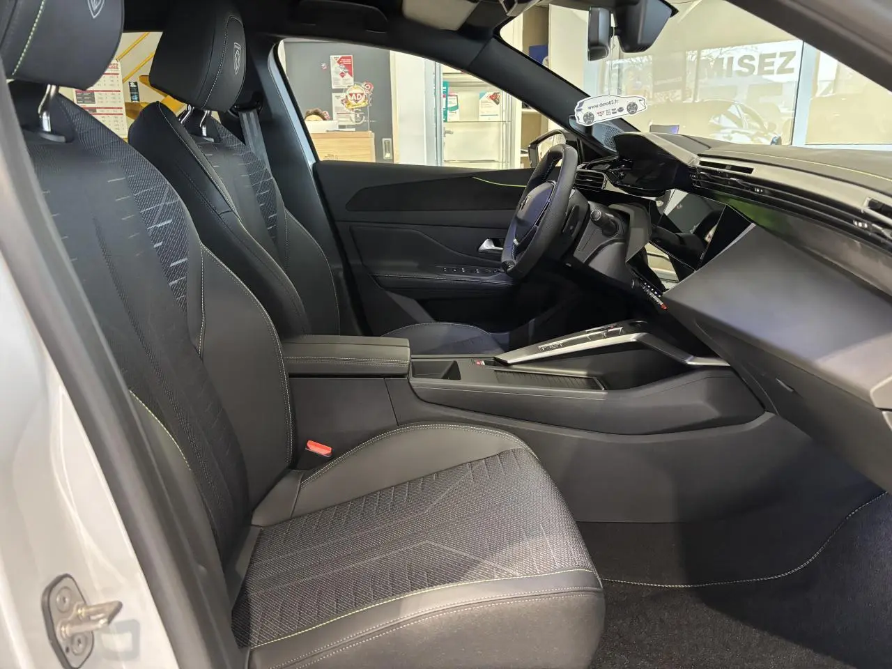 Vue intérieure côté conducteur de la Peugeot 308 Hybrid 2026 avec sellerie noire et surpiqûres vert Adamite.