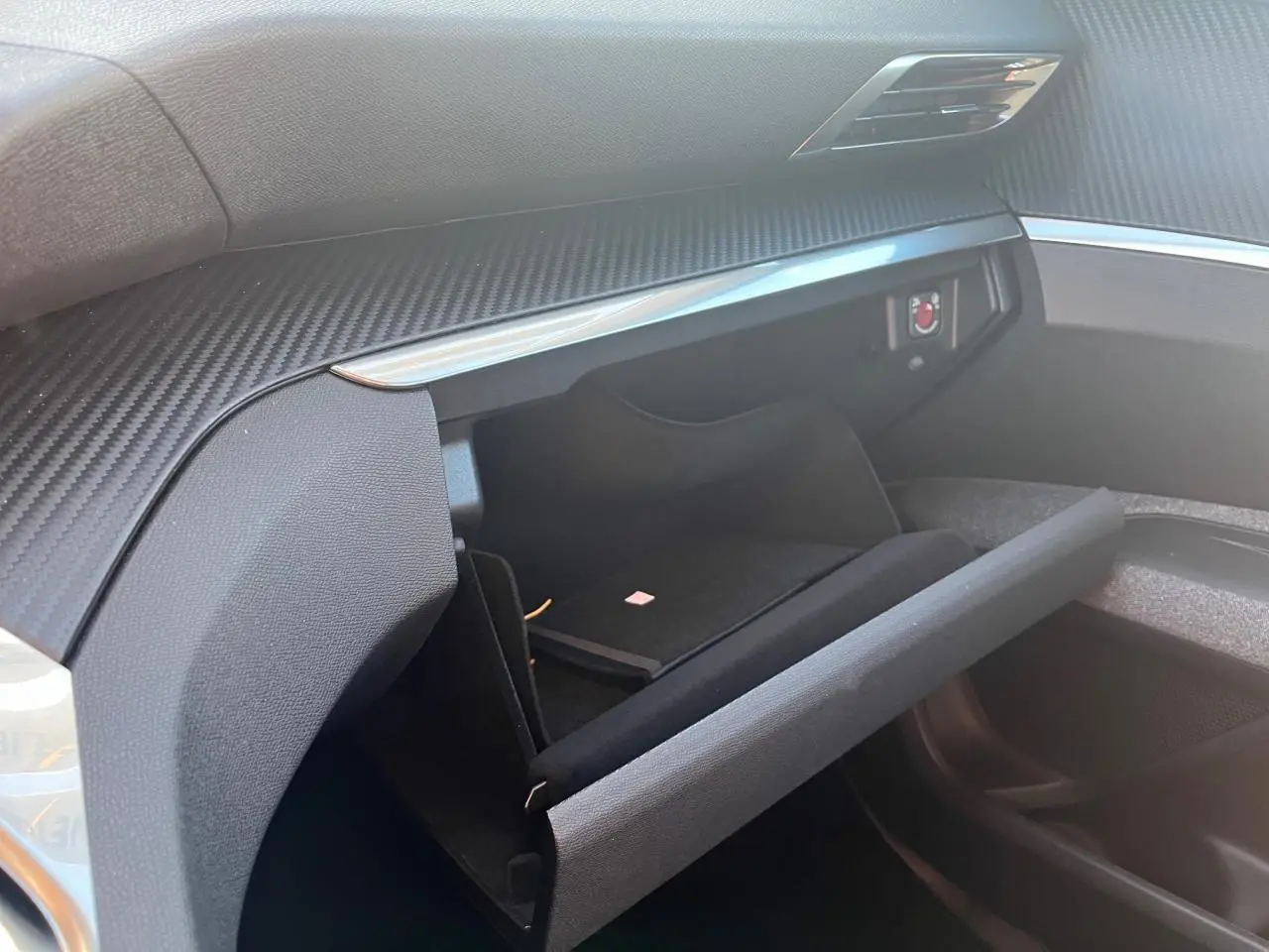 Gros plan sur la boîte à gants ouverte côté passager du Peugeot 3008 2023, intérieur noir avec finition carbone.