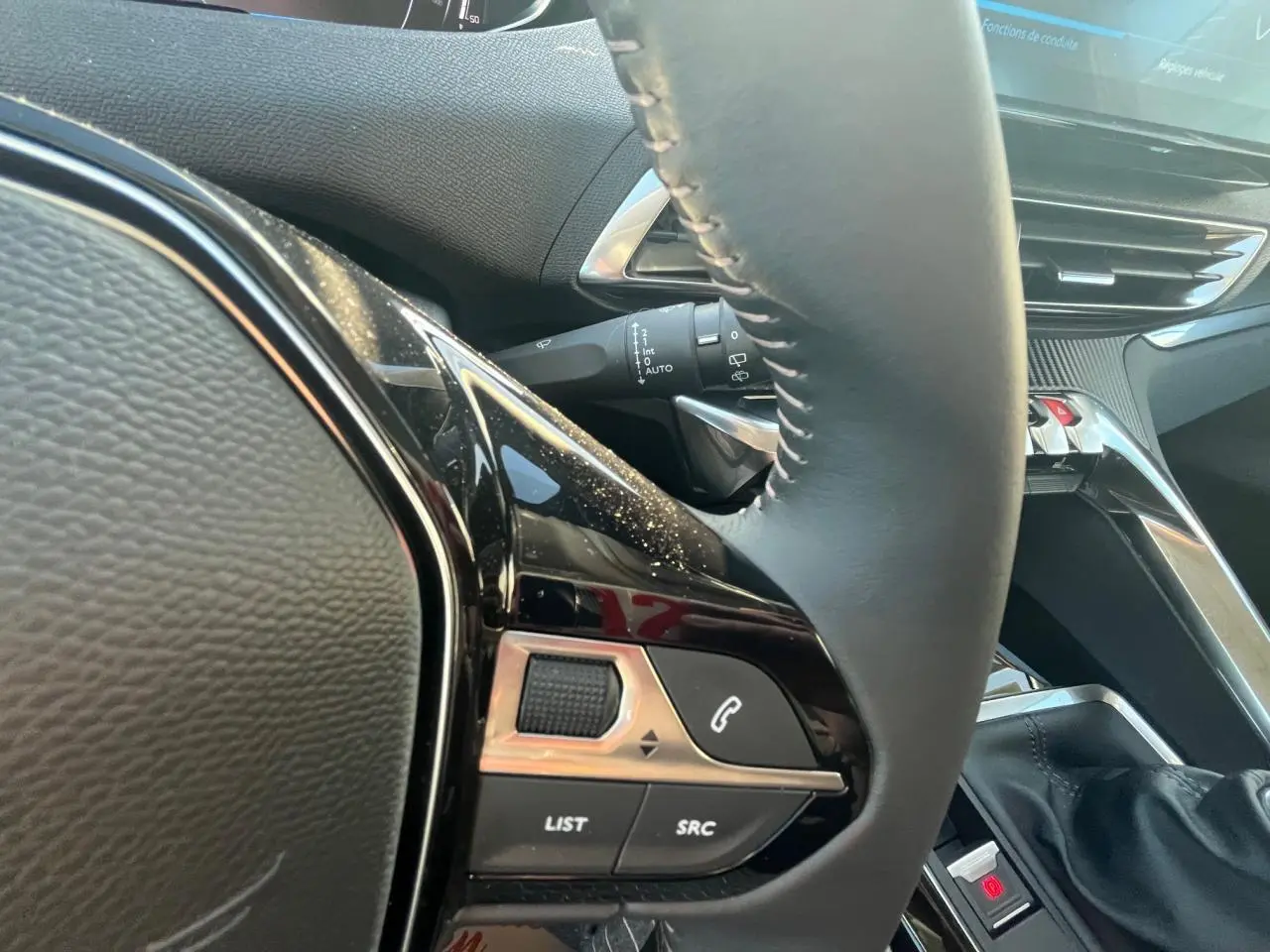 Gros plan sur le volant et la console centrale du Peugeot 3008 2023, mettant en valeur les commandes intégrées et la finition noire.