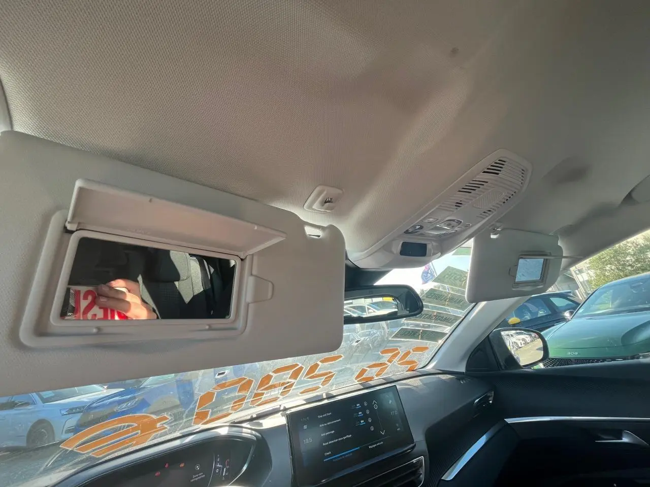 Vue intérieure du tableau de bord et pare-soleil ouvert côté conducteur d'un Peugeot 3008 gris avec écran tactile allumé.