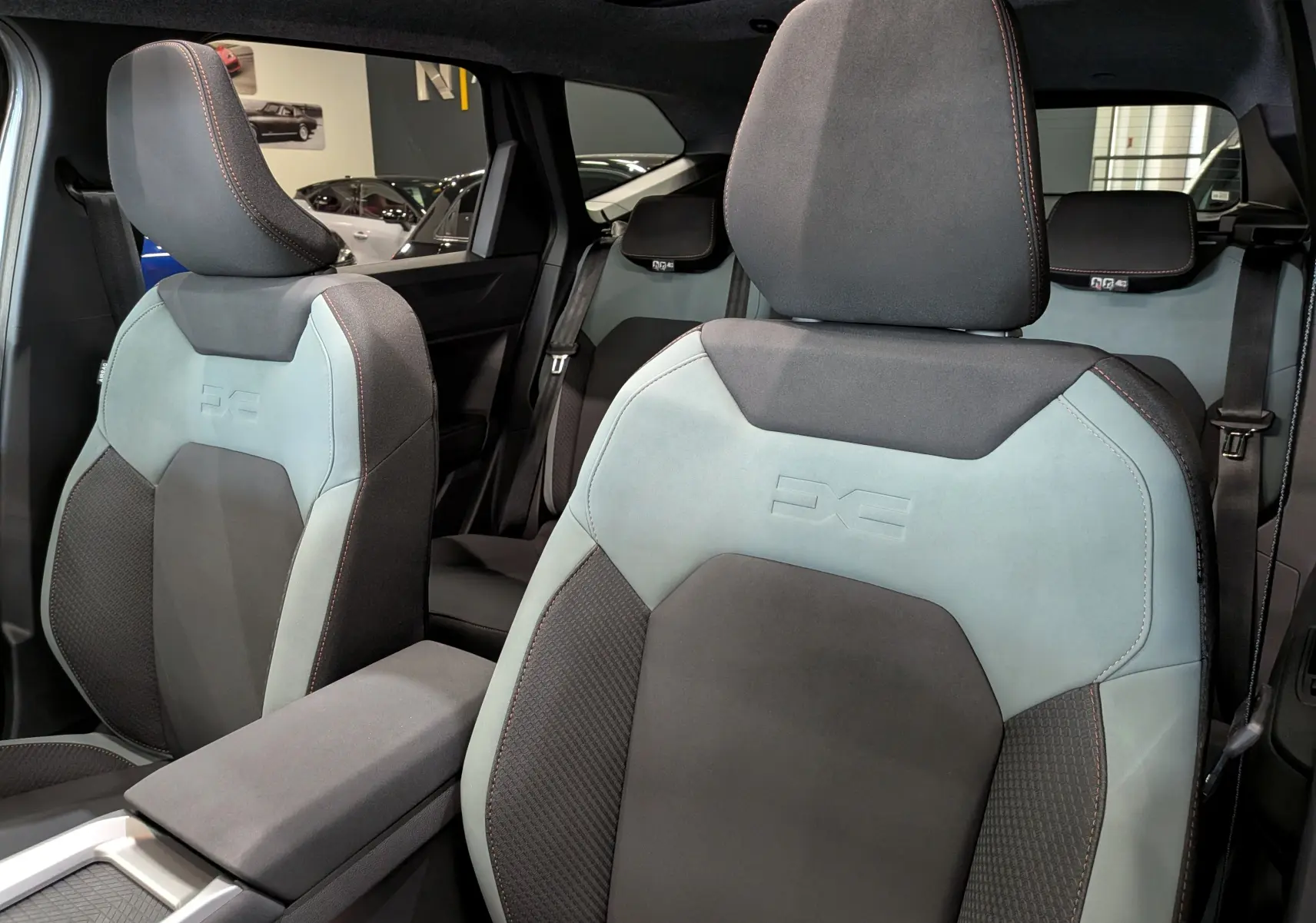 Vue intérieure rapprochée des sièges avant gris clair et noir du Dacia Bigster Hybrid-G 150 4x4 avec surpiqûres orange.