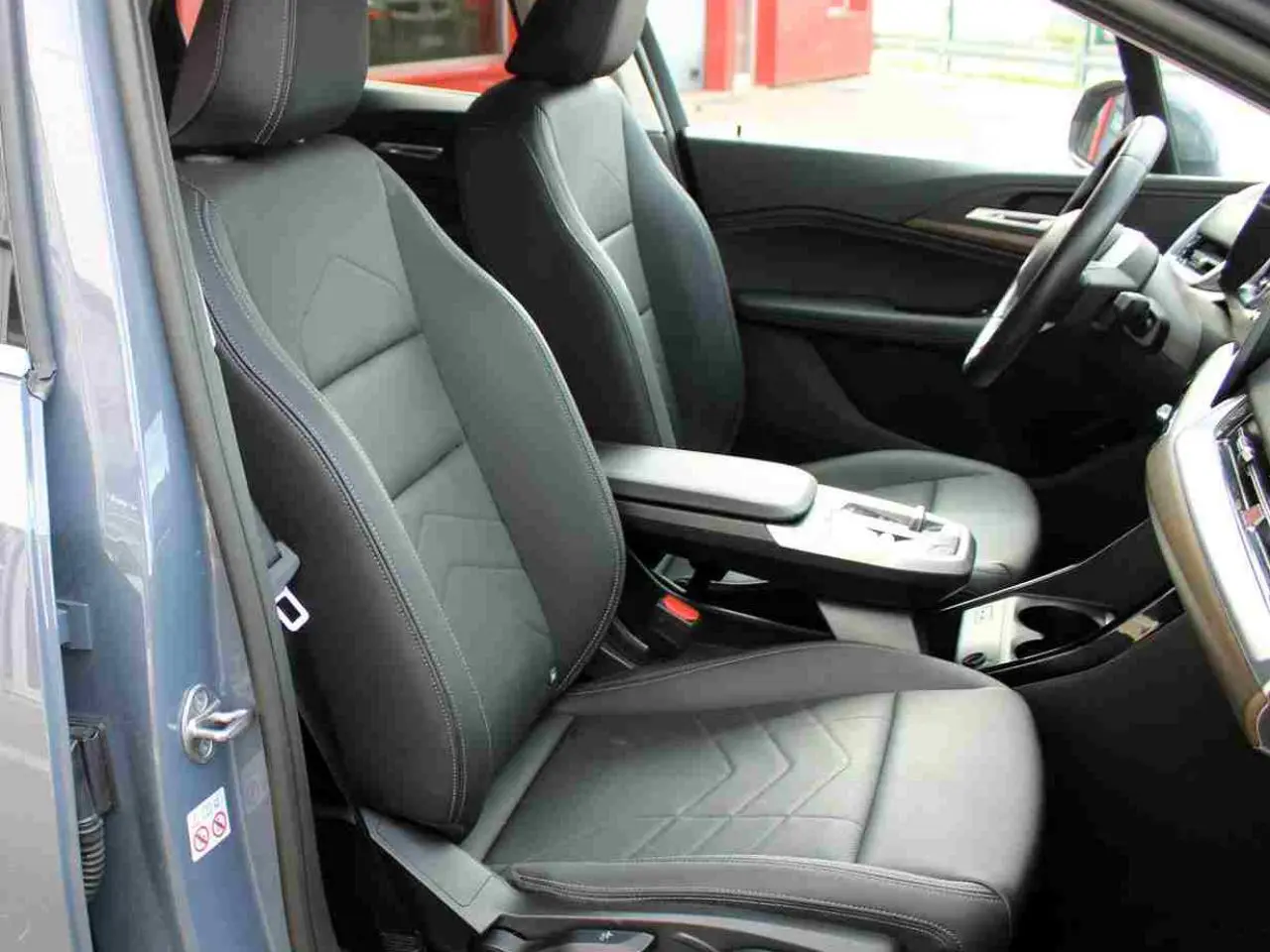 Vue intérieure côté gauche de la BMW Série 2 Active Tourer 2023, sièges simili cuir noirs et console centrale avec accoudoir.