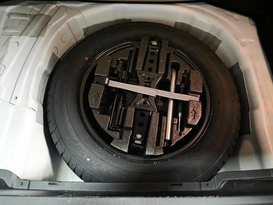 Vue rapprochée de la roue de secours noire et des outils de bord dans le coffre blanc du Skoda Kamiq 2023.