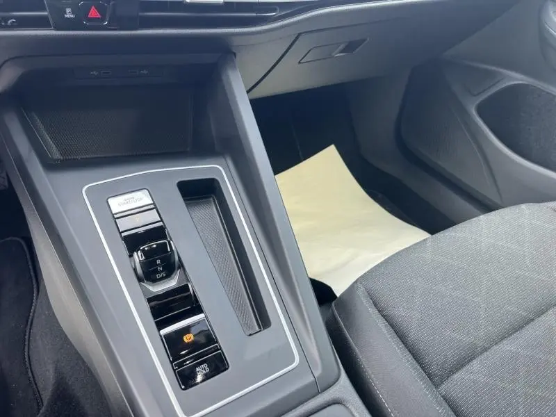 Vue rapprochée de la console centrale noire de la Volkswagen Golf 1.5 eTSI avec levier de vitesses automatique et accoudoir tissu gris.