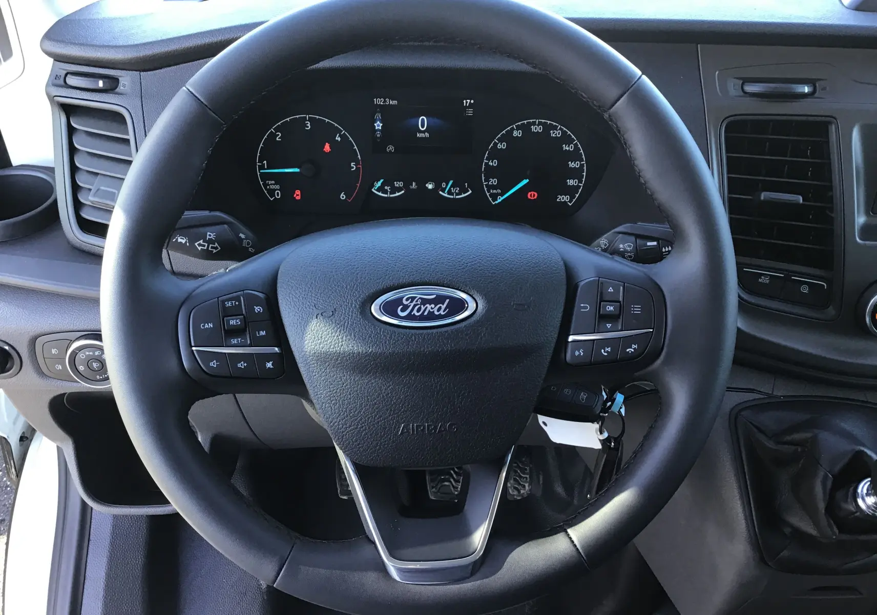 Vue rapprochée du volant multifonction noir du Ford Transit Châssis Cabine blanc, avec tableau de bord digital visible.