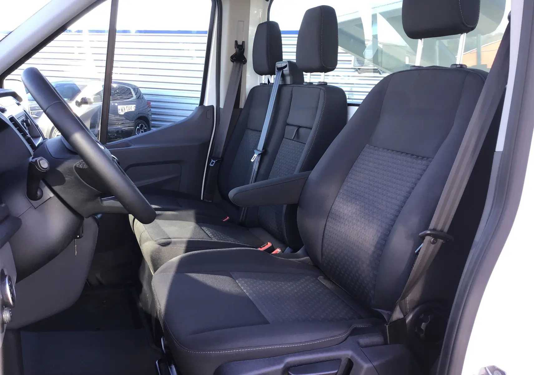 Vue intérieure côté conducteur du Ford Transit Châssis Cabine blanc 2024, montrant les sièges noirs et le volant multifonction.
