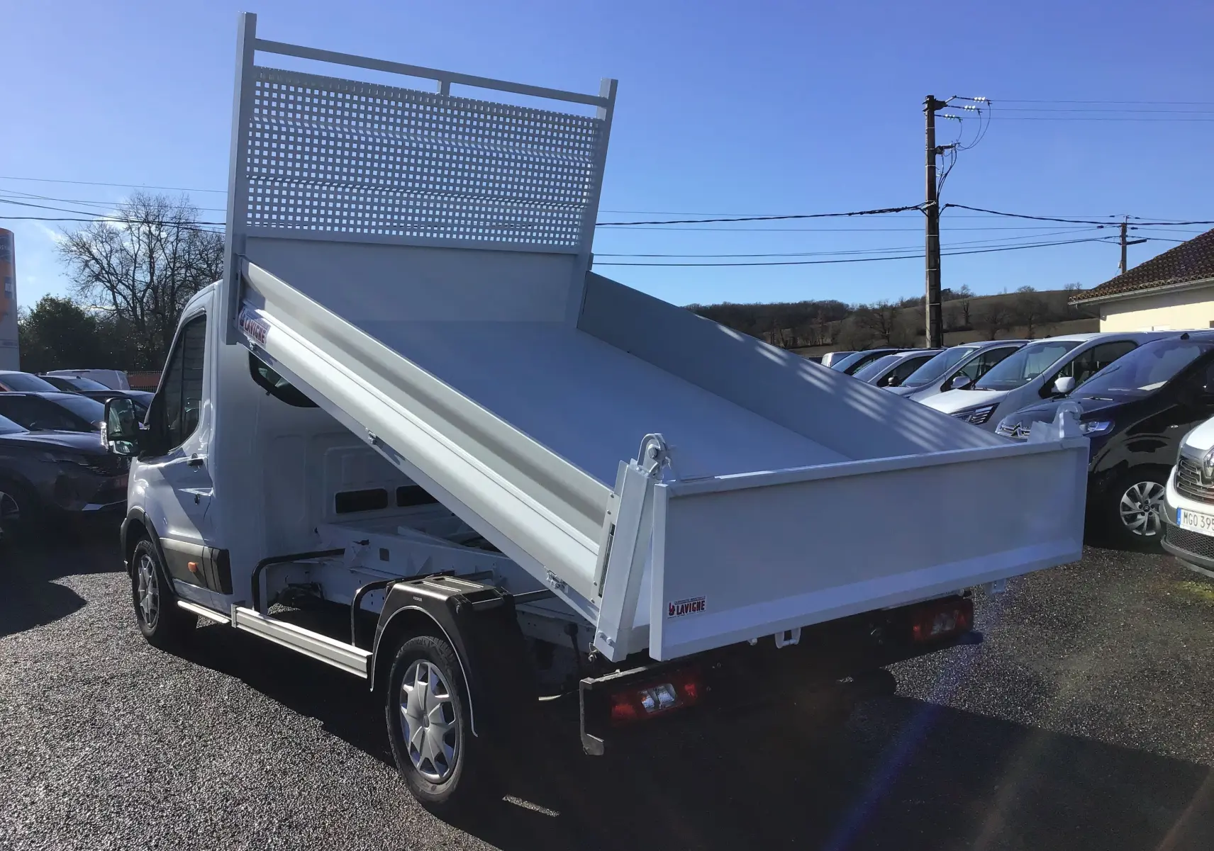 Ford Transit Chassis Cabine blanc en vue 3/4 arrière droit avec benne basculante relevée sur parking.