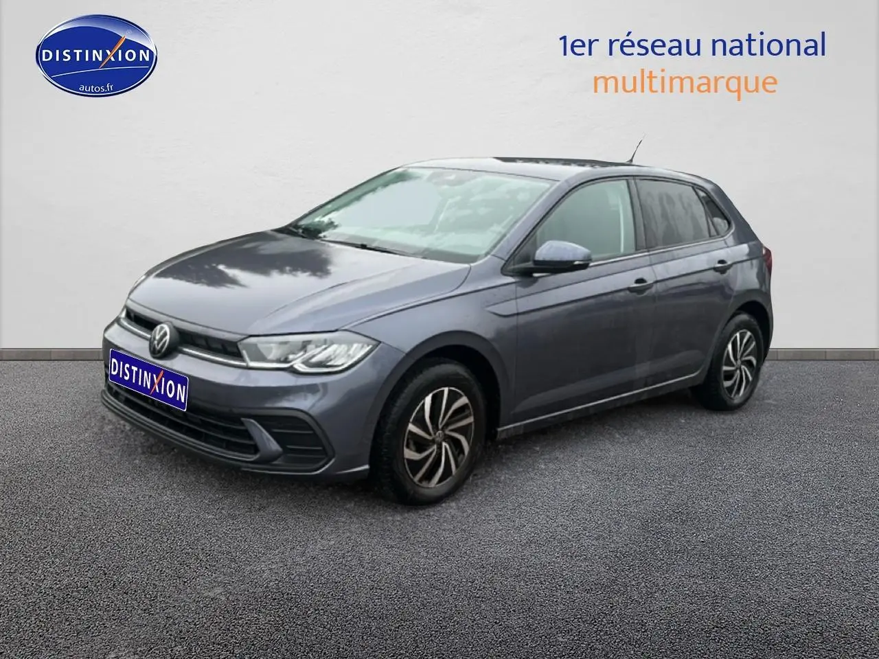 Volkswagen Polo gris cendre vue 3/4 avant droit sur sol gris avec calandre noire et jantes alliage.