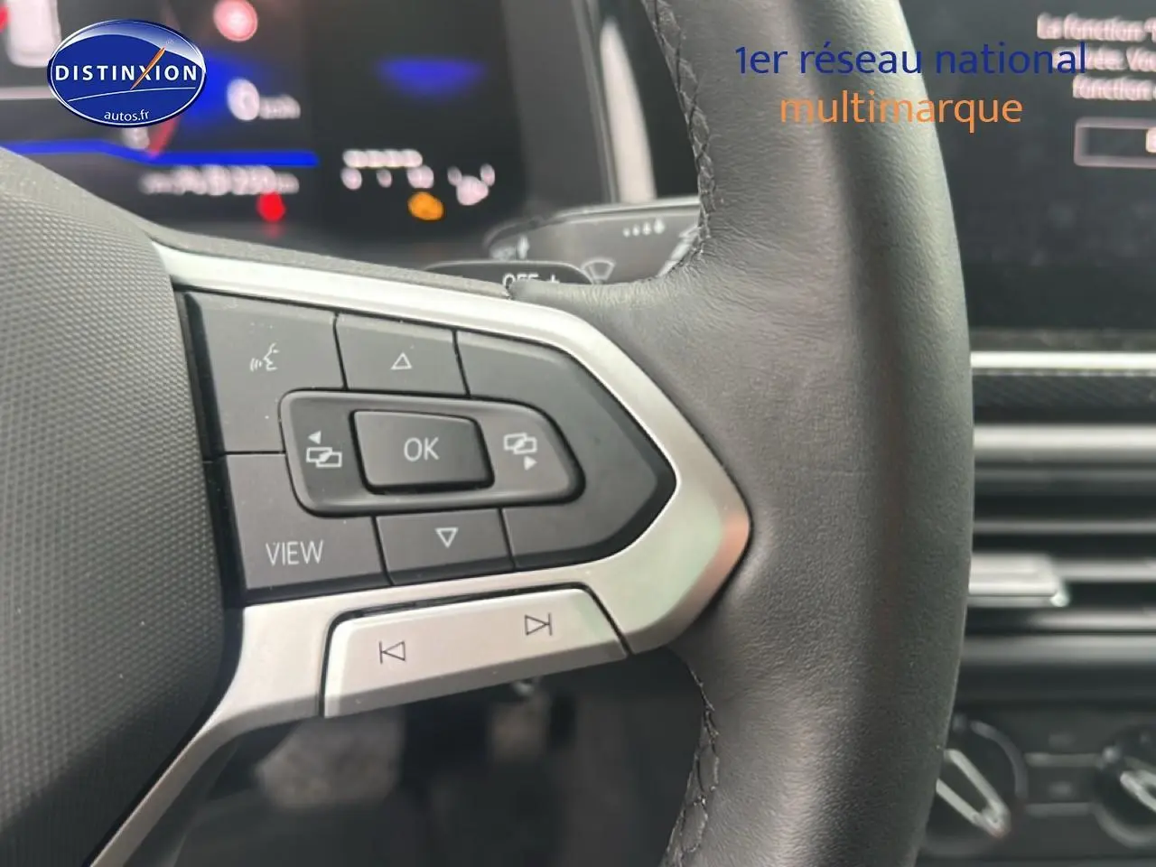 Gros plan sur les commandes multifonctions à gauche du volant cuir d’une Volkswagen Polo gris cendre, tableau de bord numérique visible.