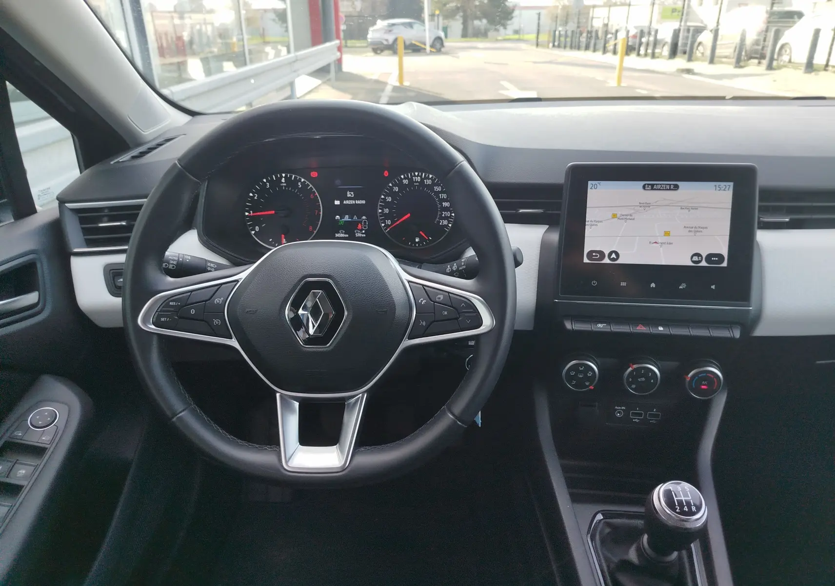 Vue intérieure avant centrée sur le volant Renault, tableau de bord noir avec écran tactile et levier de vitesse manuel.