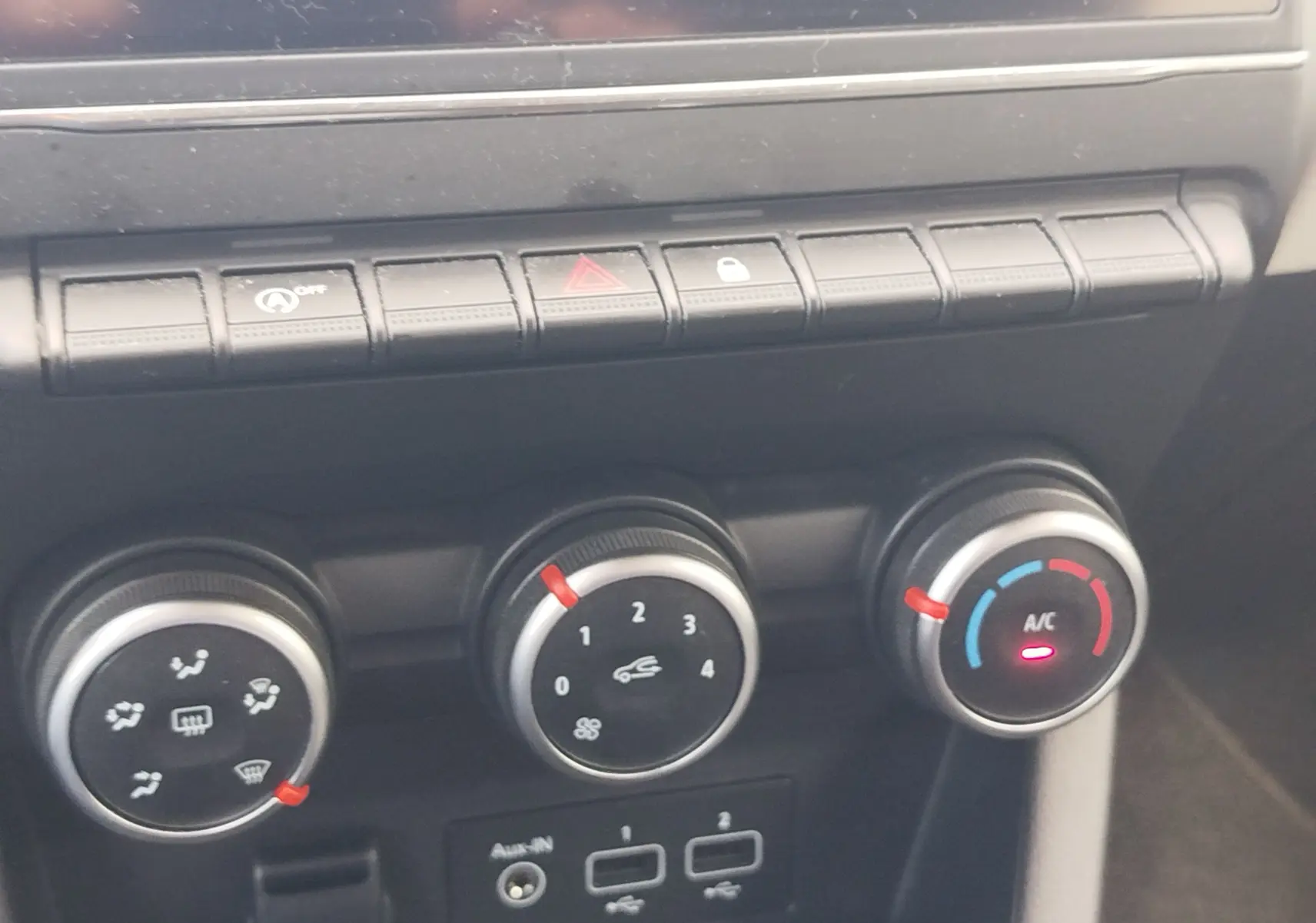 Gros plan sur les commandes de climatisation et boutons de fonction du tableau de bord d’une Renault Clio bleu Iron.