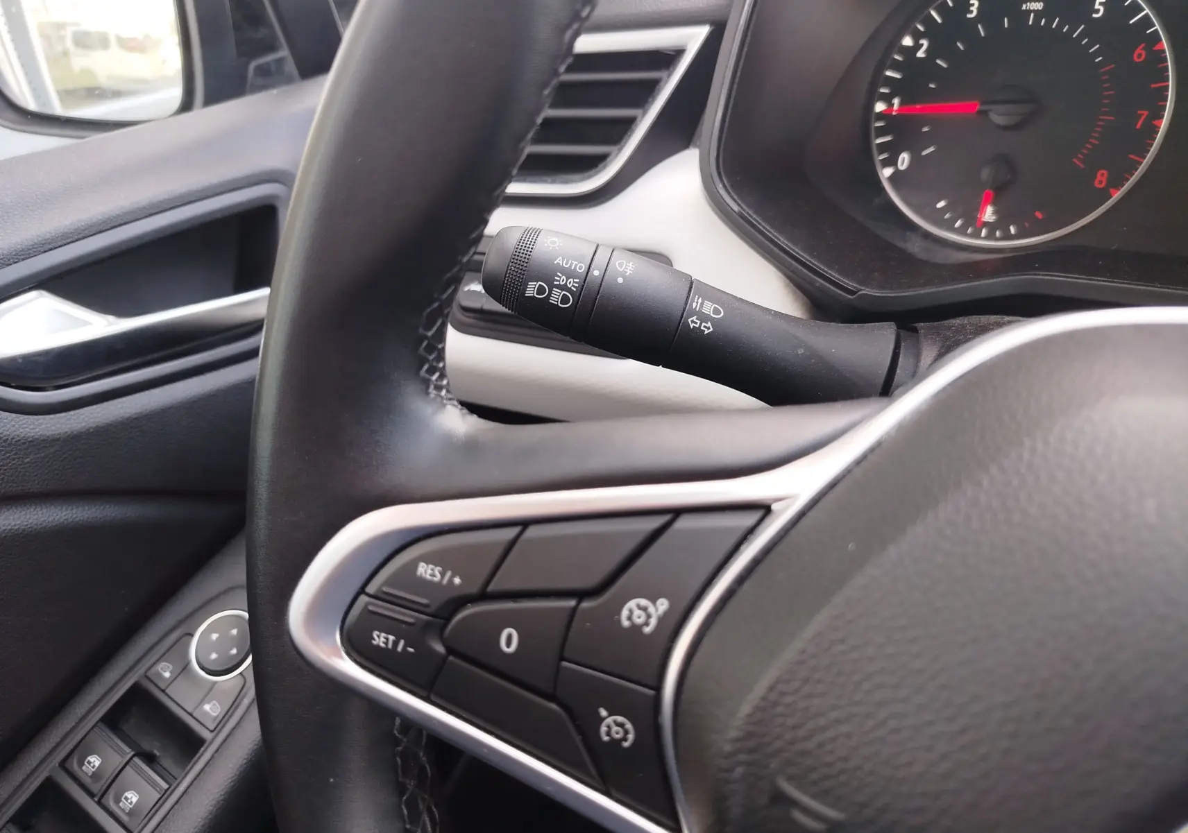 Vue rapprochée du volant côté gauche d’une Renault Clio 2022 bleu Iron, avec commandes au volant et commodo d’éclairage visibles.