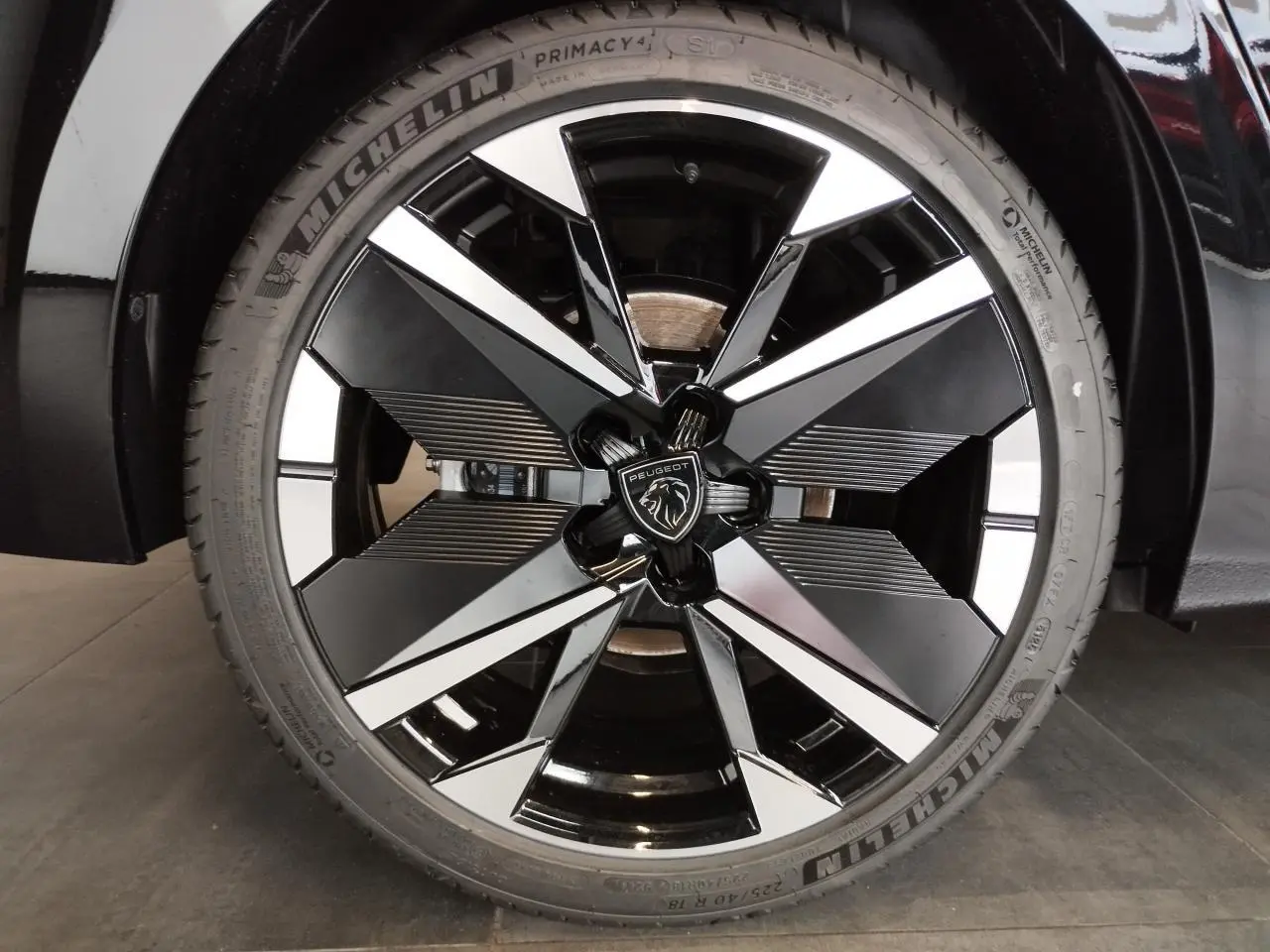 Gros plan sur la jante alliage 18" bi-tons noir et argent avec logo Peugeot, sur roue avant d'une 308 noire.