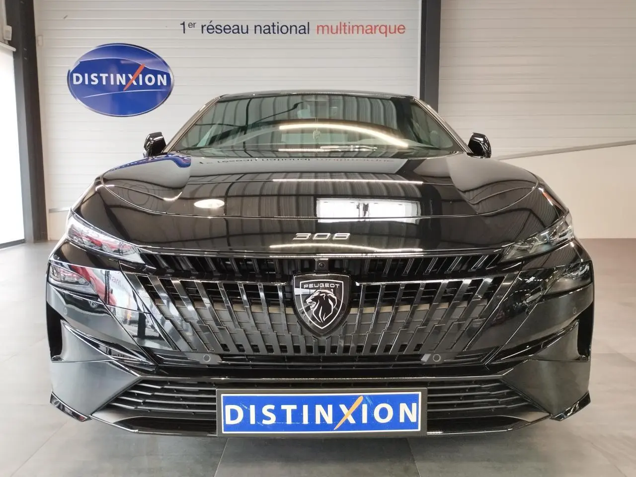 Vue avant d'une Peugeot 308 noire métallisée avec calandre et blason Peugeot lumineux, en intérieur showroom.