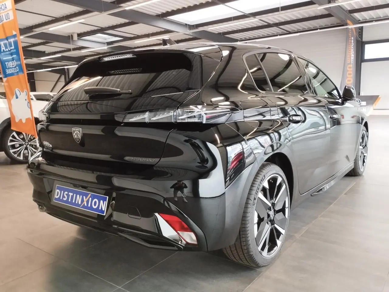 Vue 3/4 arrière droite d'une Peugeot 308 Hybrid noire métallisée avec jantes alliage bi-tons et feux arrière LED distinctifs.