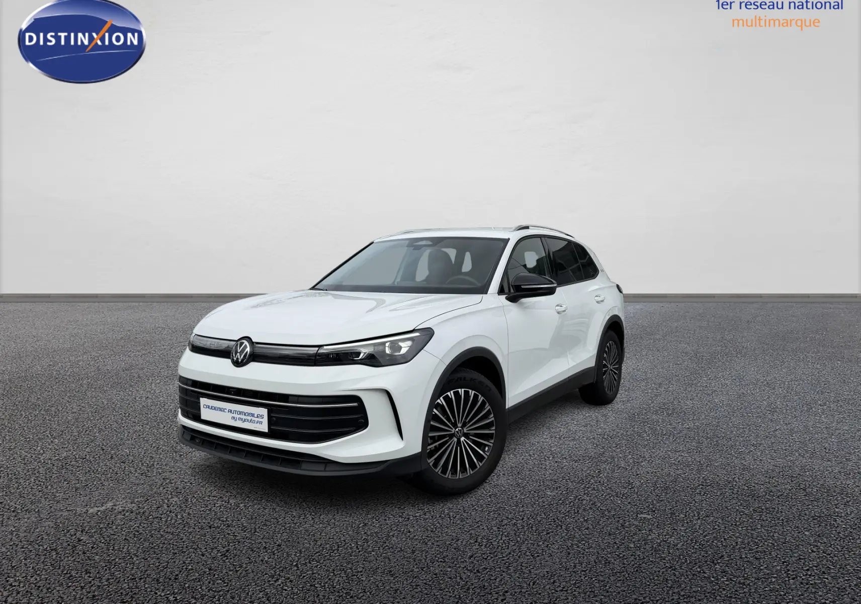 Volkswagen Tiguan blanc vu en 3/4 avant droit, avec jantes noires et calandre noire brillante, devant un concessionnaire.