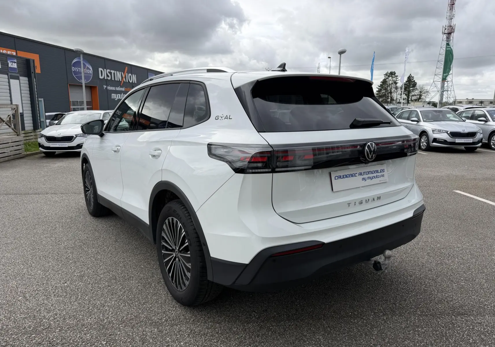 Vue 3/4 arrière droite du Volkswagen Tiguan blanc 2025 avec attelage rabattable et vitres arrière teintées.