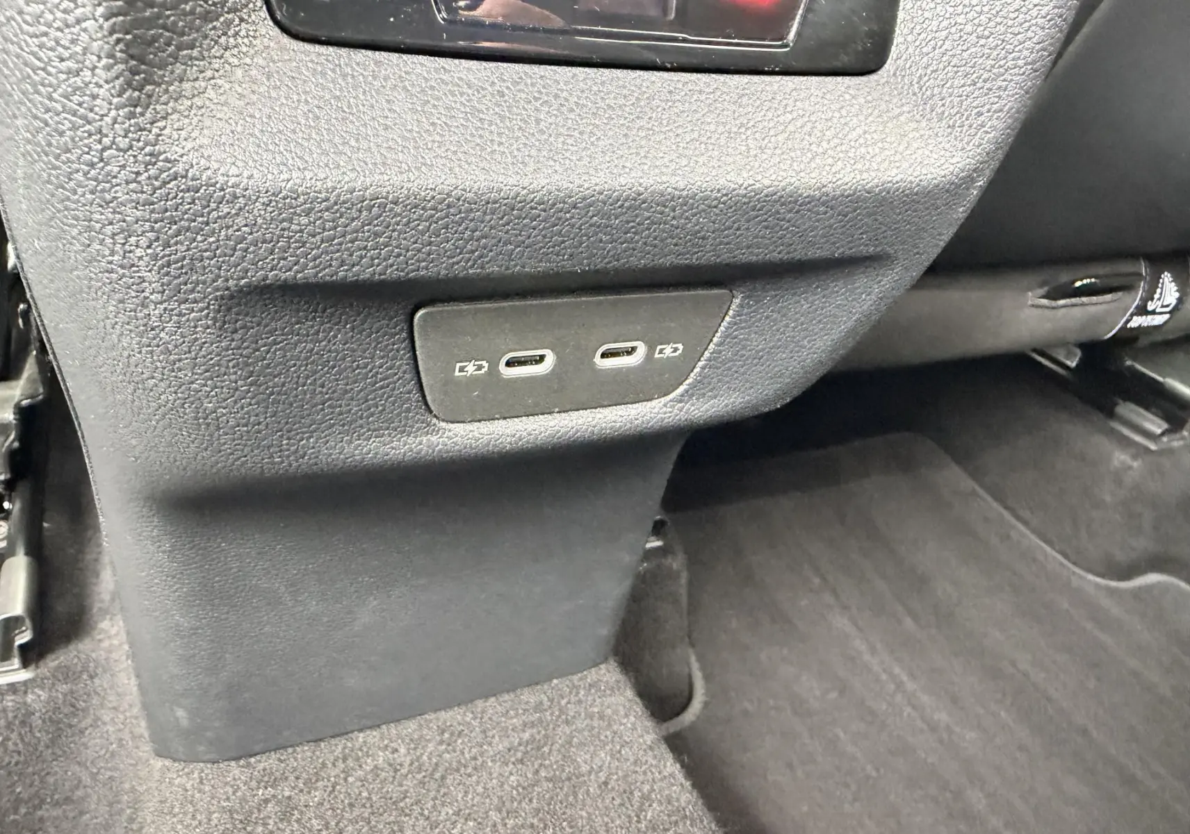 Gros plan sur les ports USB-C arrière du Volkswagen Tiguan 2025, intérieur noir avec moquette sombre.