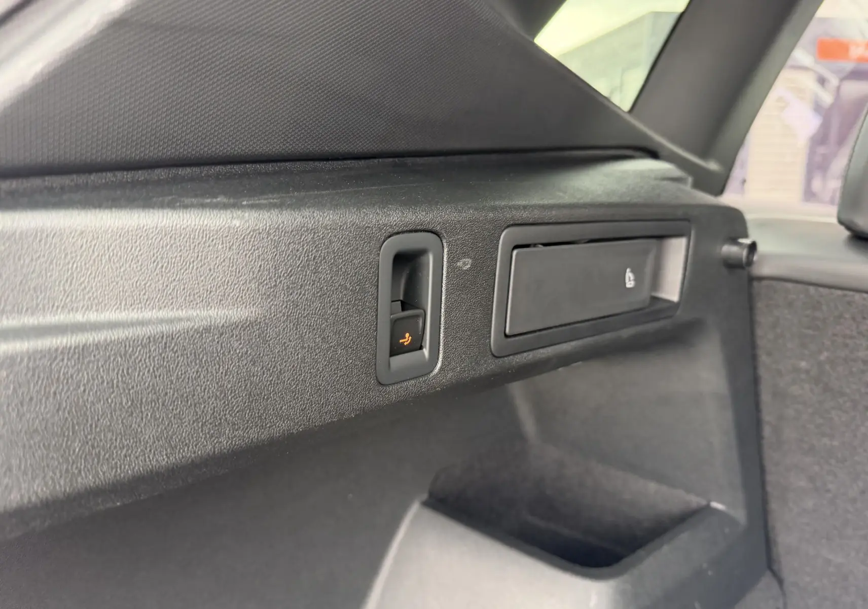 Détail intérieur du coffre du Volkswagen Tiguan 2025, montrant la commande électrique de rabattement des sièges en plastique noir.