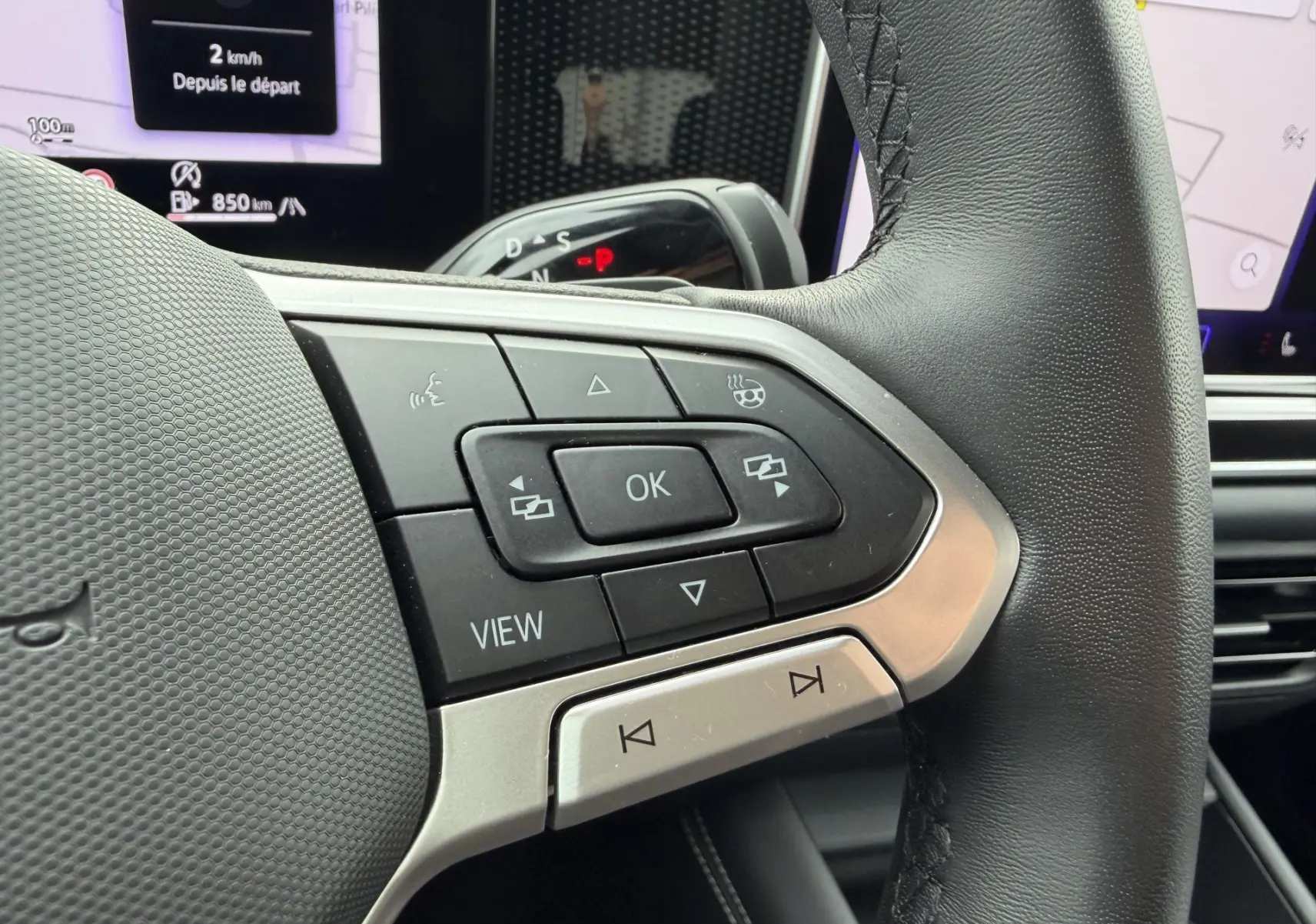 Gros plan sur les commandes multifonctions côté gauche du volant cuir noir du Volkswagen Tiguan 2025 avec écran digital en arrière-plan.