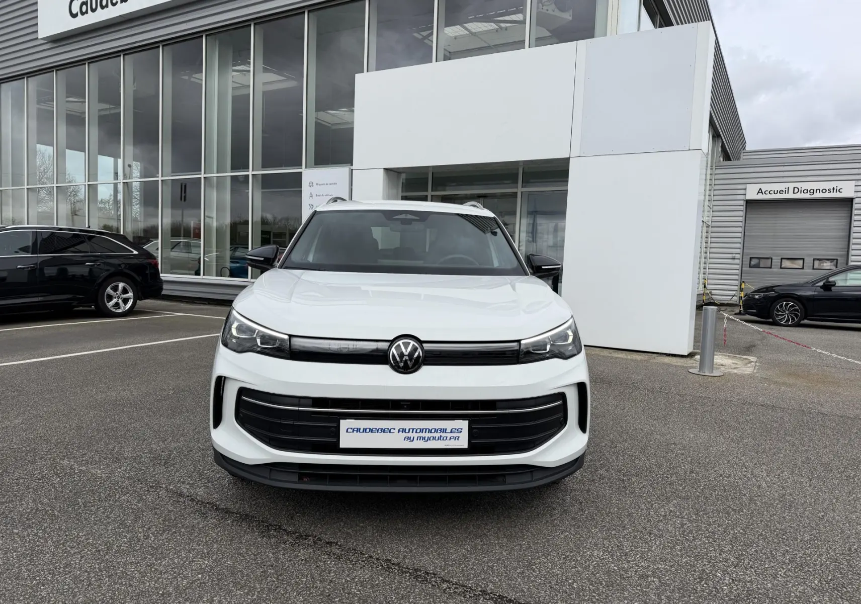 Vue de face d’un Volkswagen Tiguan blanc 2025 stationné devant un bâtiment commercial avec calandre noire et phares LED.