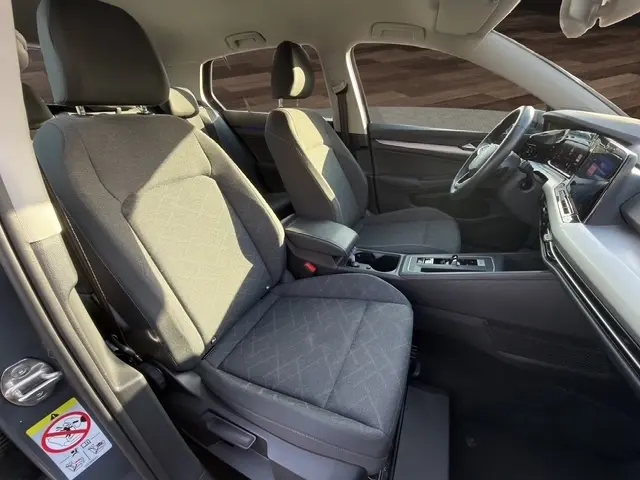 Vue intérieure côté gauche de la Volkswagen Golf 2023 gris clair, montrant les sièges avant et le tableau de bord moderne.