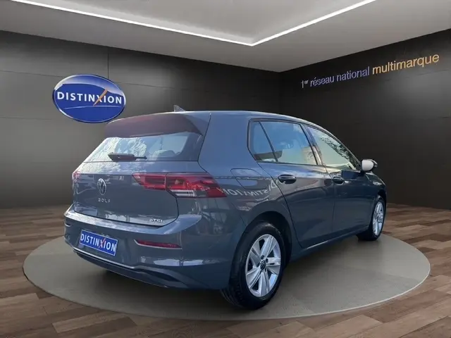 Vue 3/4 arrière droite d'une Volkswagen Golf gris clair 2023 avec feux LED et caméra de recul en showroom.