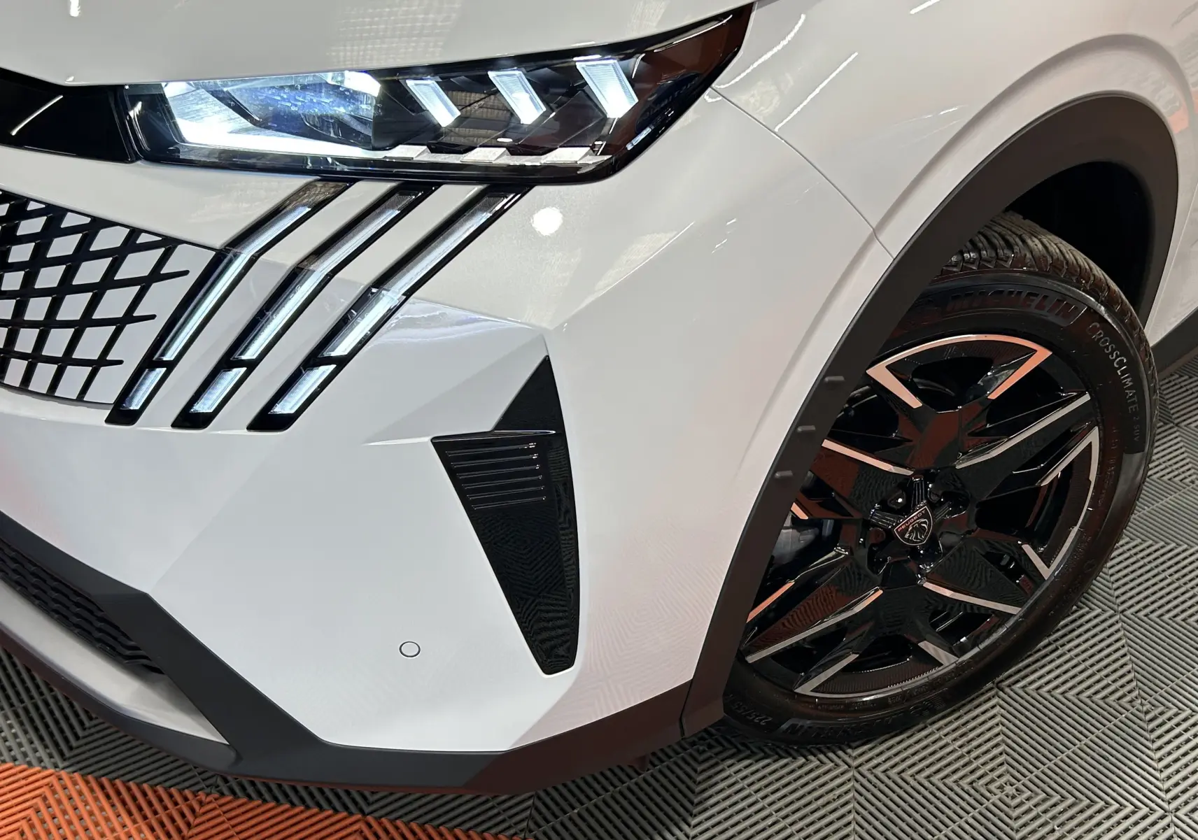 Gros plan sur l’avant droit blanc Okenite du Peugeot 3008 III Hybrid avec feux LED et jante noire biton.