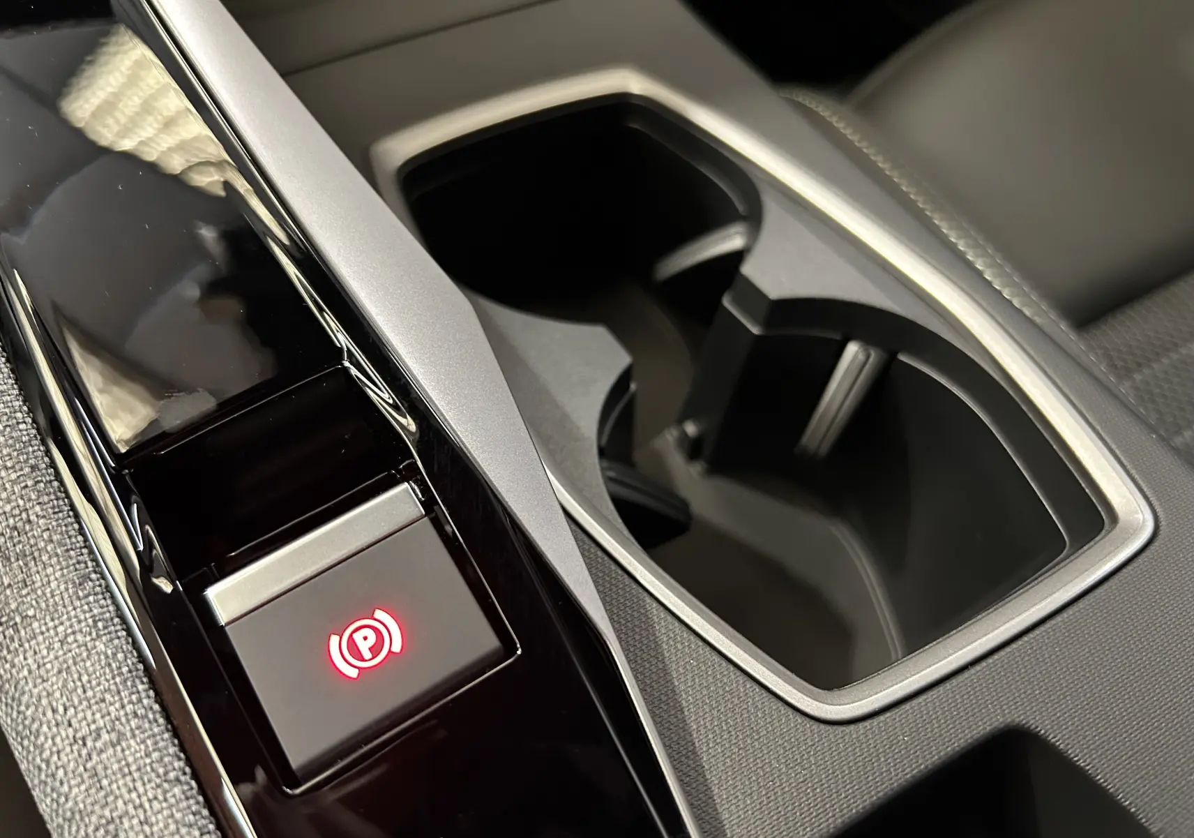 Gros plan sur la console centrale noire et grise du Peugeot 3008 Hybrid, avec bouton de frein à main électronique éclairé en rouge.