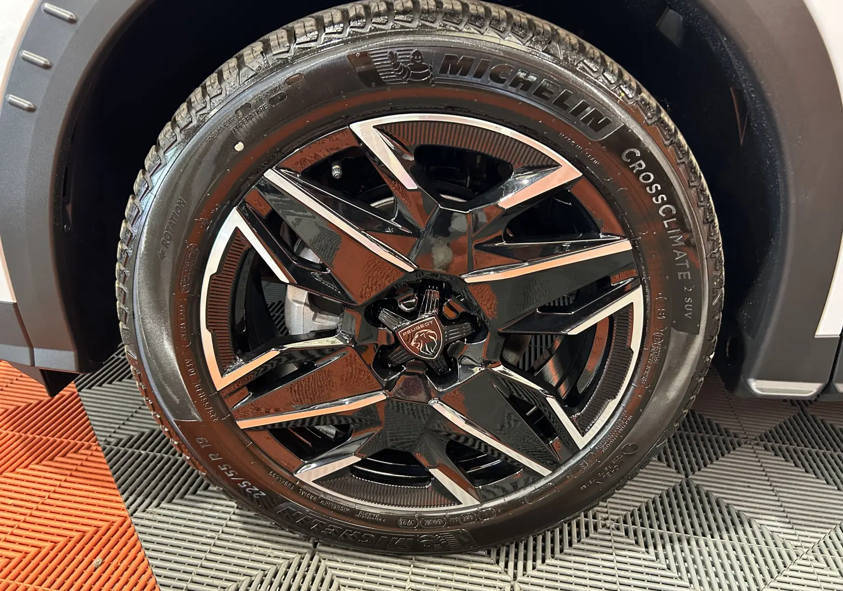 Gros plan sur la roue avant droite du Peugeot 3008 Hybrid blanc Okenite avec jante alliage noire et inserts chromés.