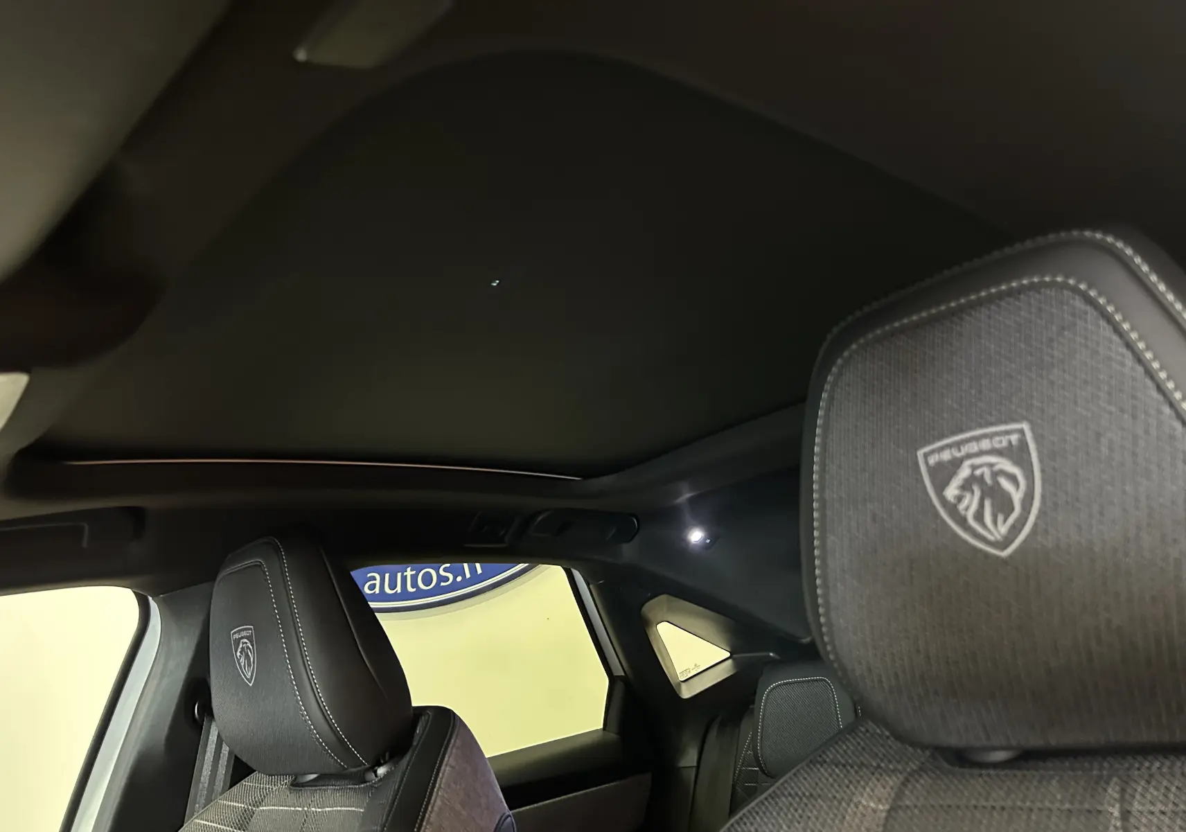 Vue intérieure du Peugeot 3008 Hybrid 2026, montrant les appuis-tête avant avec logo Peugeot brodé et toit ouvrant panoramique noir.