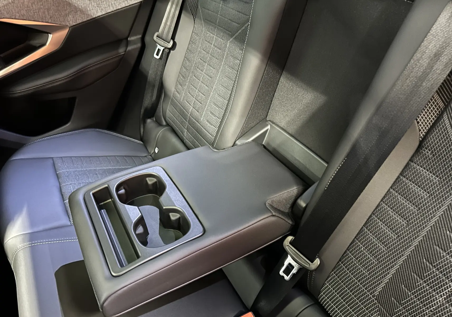 Vue rapprochée de l’accoudoir central arrière noir avec porte-gobelets sur les sièges arrière gris foncé du Peugeot 3008 Hybrid.