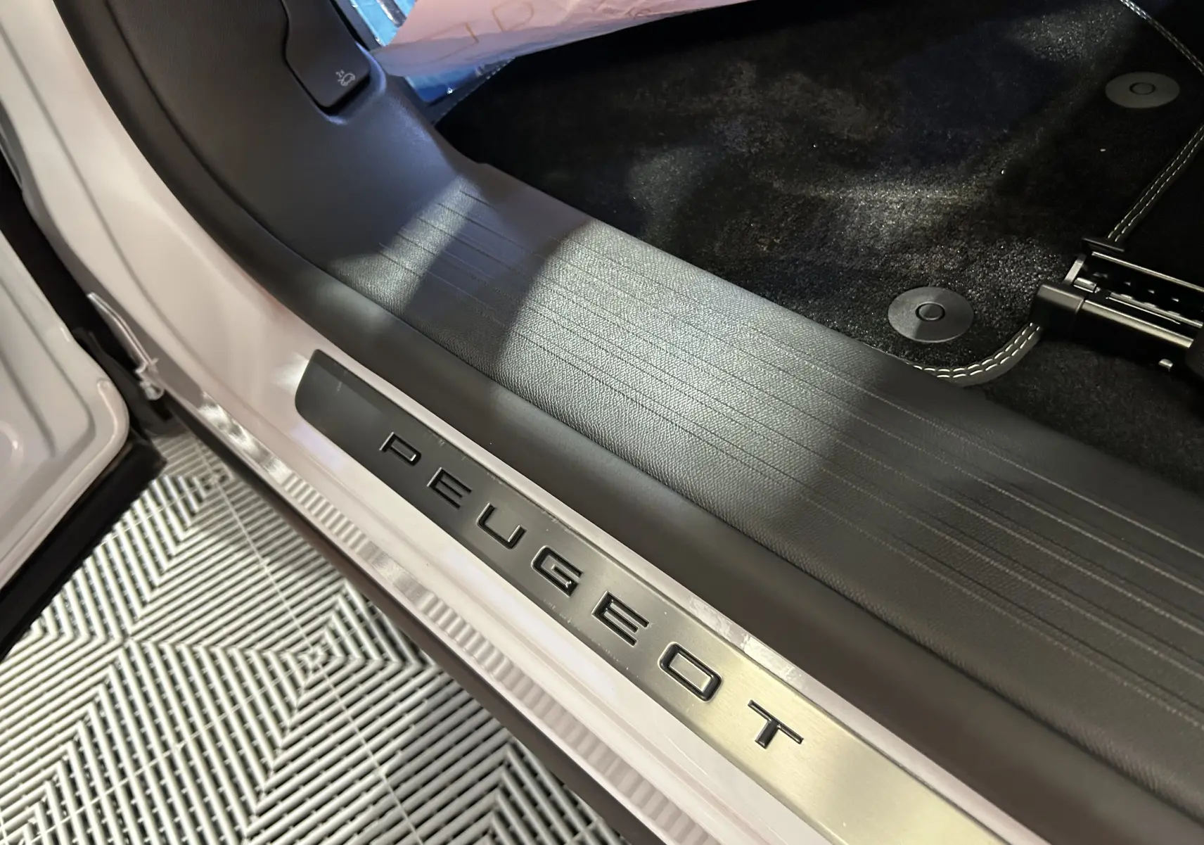 Gros plan sur la plaque de seuil de porte avec logo Peugeot sur un Peugeot 3008 blanc Okenite, côté intérieur avant droit.