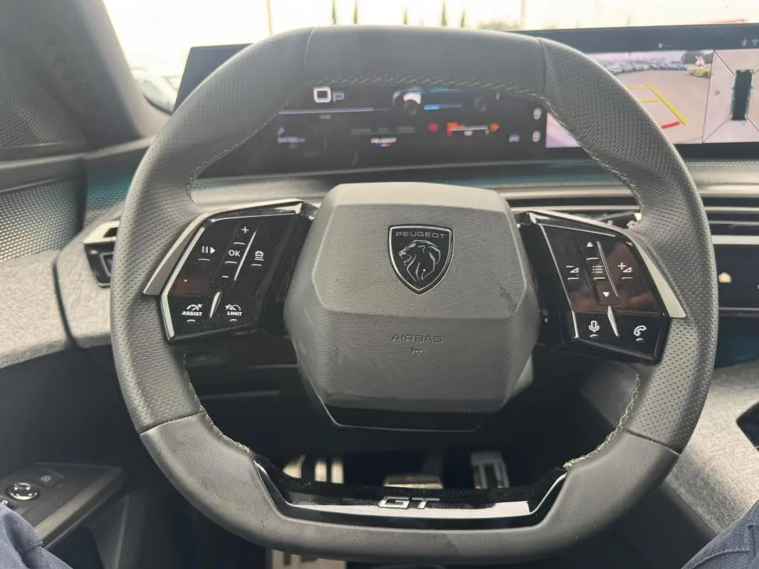Vue rapprochée du volant noir du Peugeot 5008 Hybrid GT 2025 avec commandes intégrées et logo central.