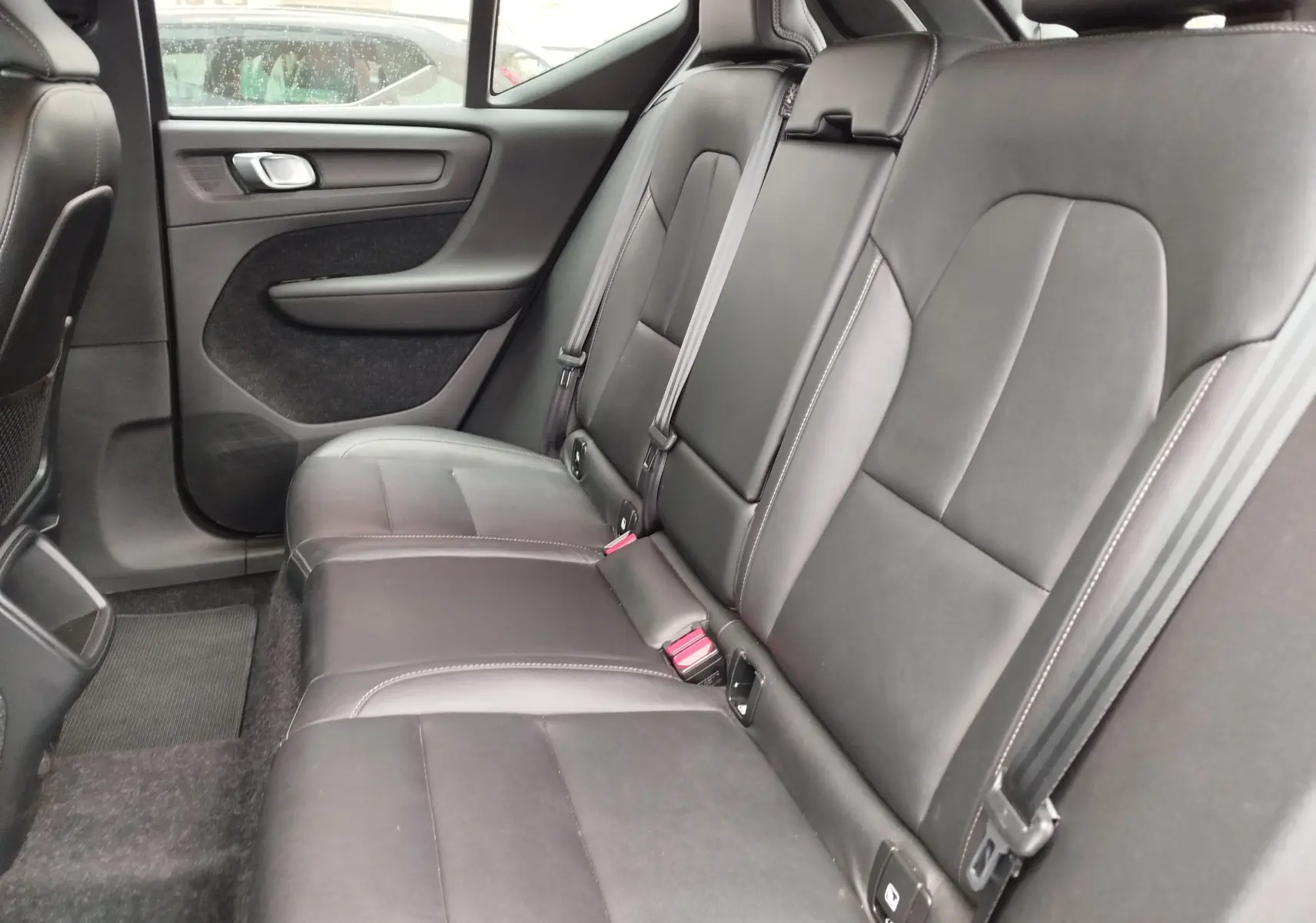 Vue intérieure côté droit des sièges arrière en cuir noir du Volvo XC40 beige, mettant en valeur les ceintures de sécurité et les finitions.