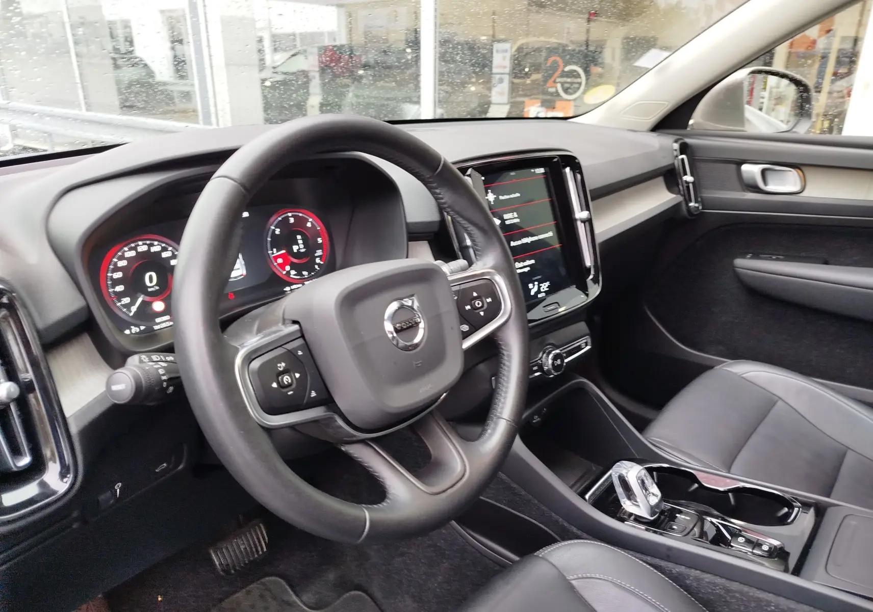 Vue intérieure côté conducteur du Volvo XC40 beige, avec tableau de bord numérique et écran tactile central.